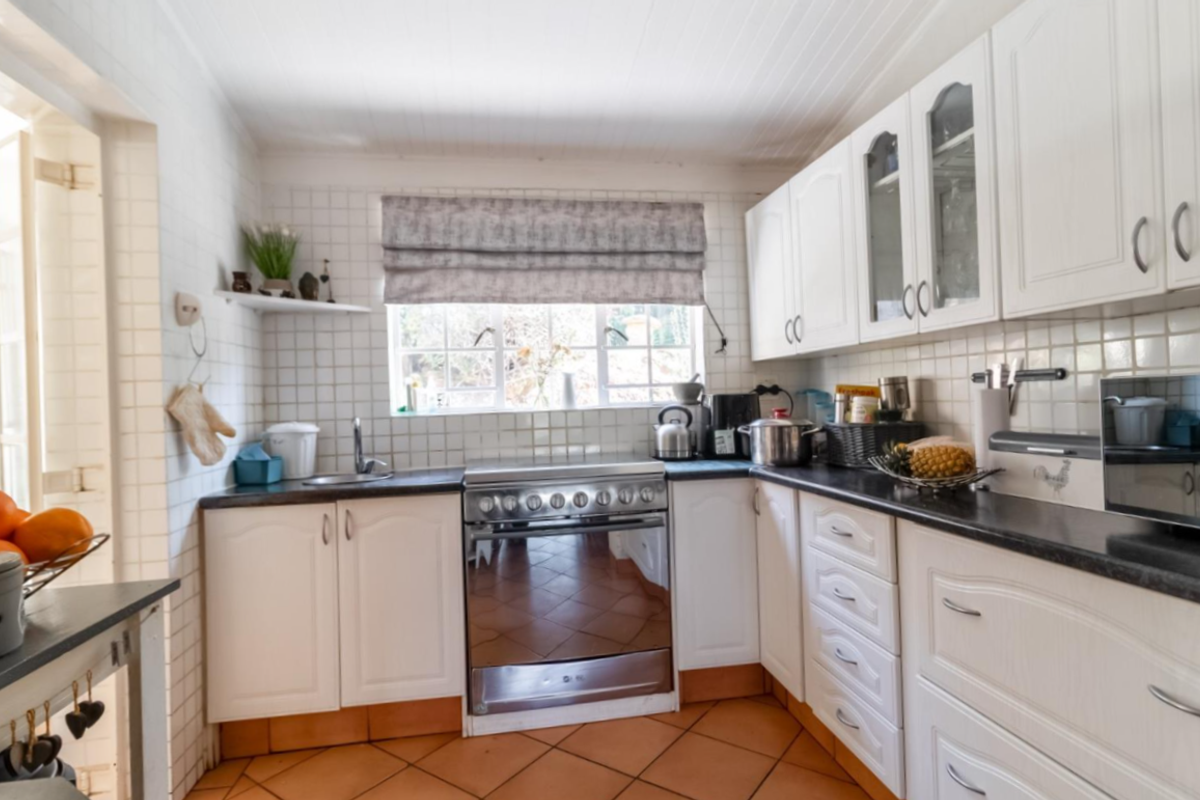 A functional kitchen featuring white cabinetry, tiled splashbacks, a stainless steel stove, and terracotta-style floor tiles with ample counter space.