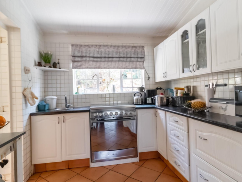 A functional kitchen featuring white cabinetry, tiled splashbacks, a stainless steel stove, and terracotta-style floor tiles with ample counter space.