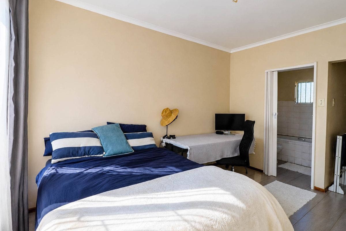 A bedroom featuring laminate flooring, neutral wall tones, and an en-suite bathroom accessible via a folding door.