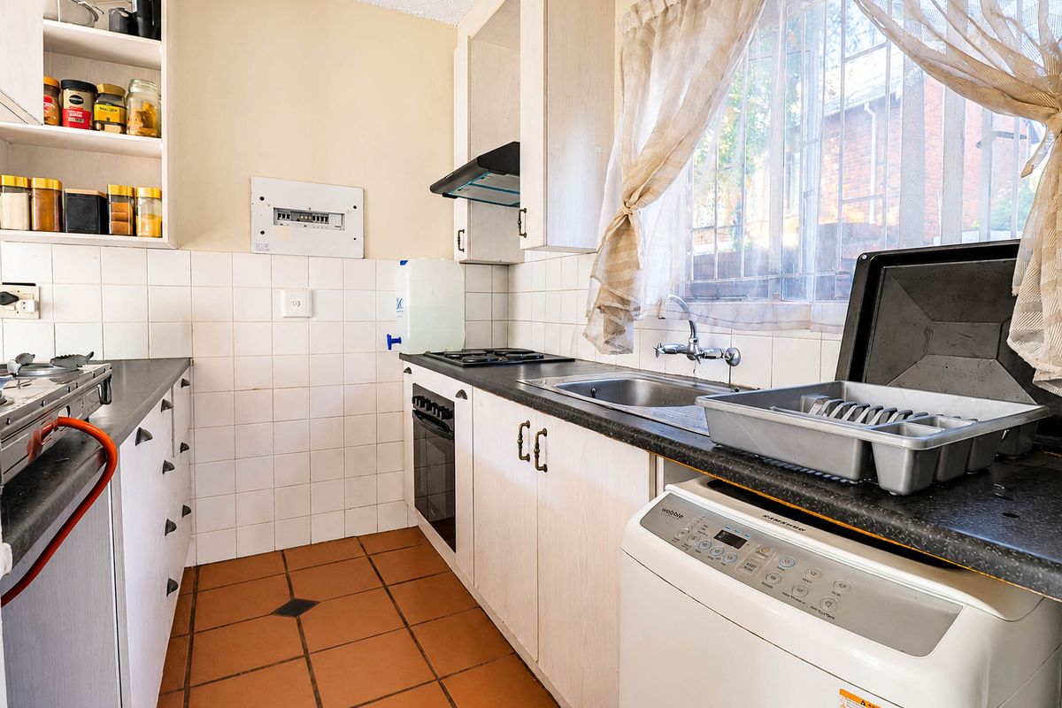 Functional kitchen featuring built-in cabinetry, gas hob, oven, extractor fan, and tiled flooring with a window providing natural light.