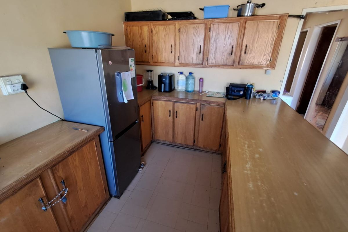A dated kitchen featuring wooden cabinetry, laminate countertops, and tiled flooring, offering a functional layout with potential for modernization.