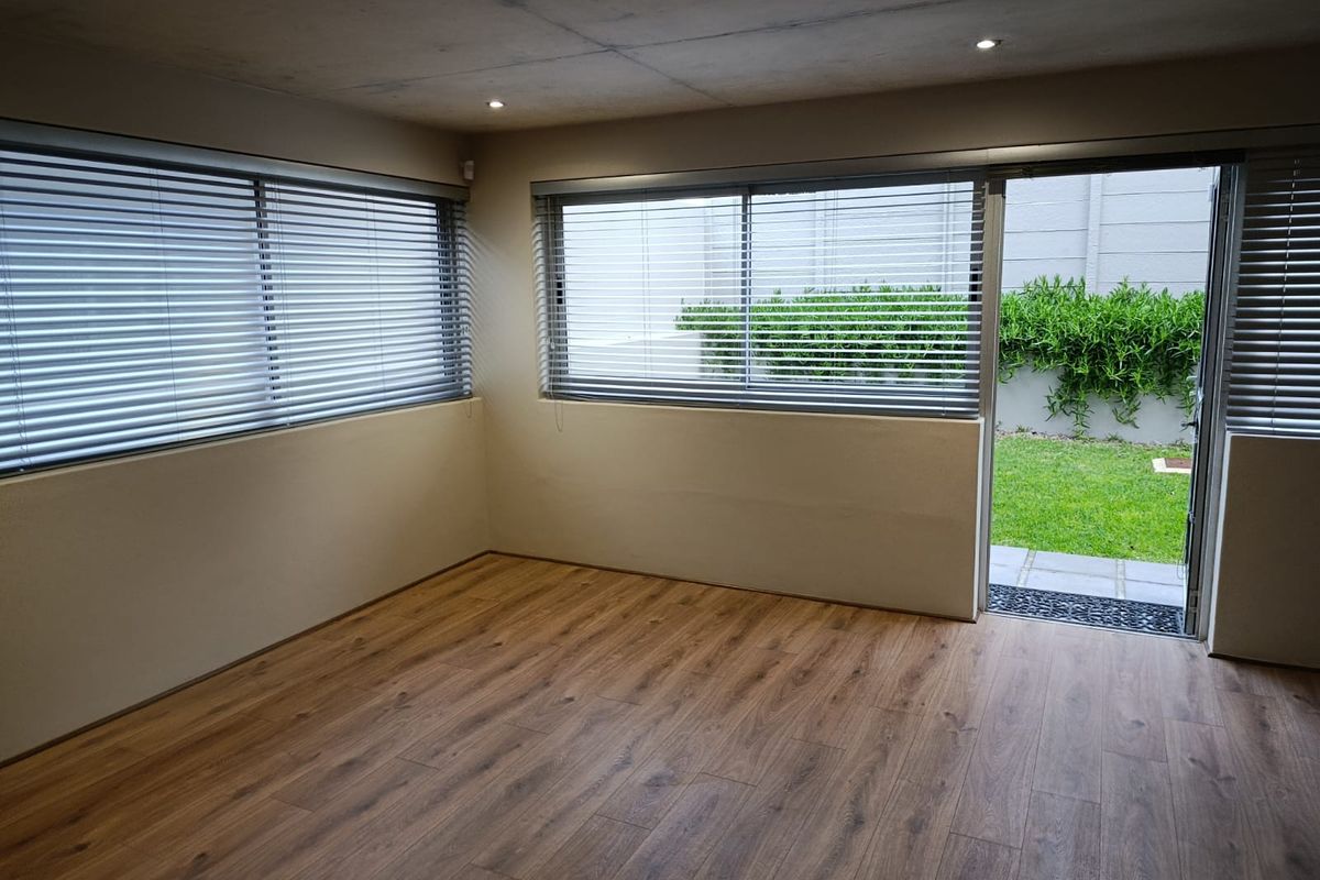 An empty, well-lit living room featuring modern laminate flooring, recessed downlights, and a sliding glass door providing direct access to the rear garden.