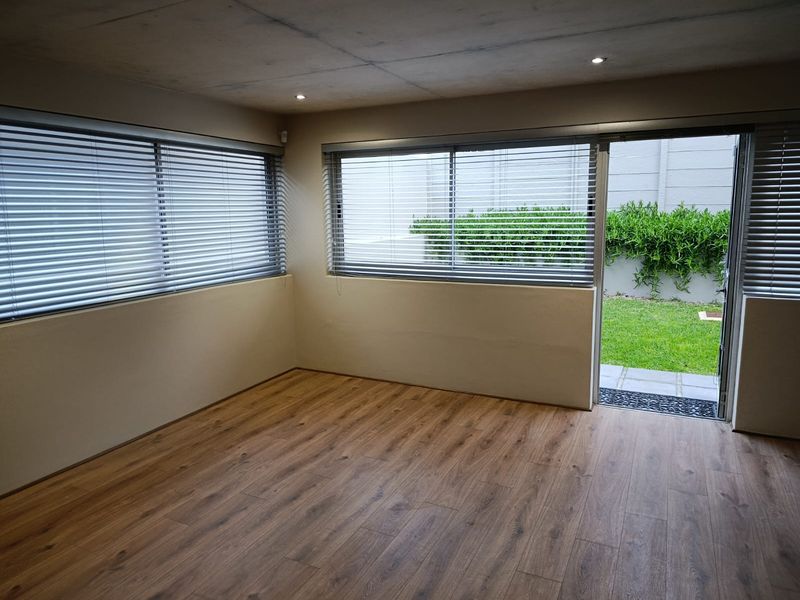 An empty, well-lit living room featuring modern laminate flooring, recessed downlights, and a sliding glass door providing direct access to the rear garden.