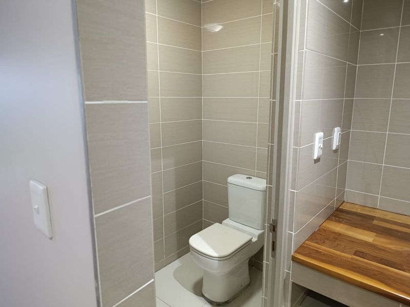 A clean, modern bathroom featuring neutral wall tiles, a white toilet, and a wooden countertop surface.