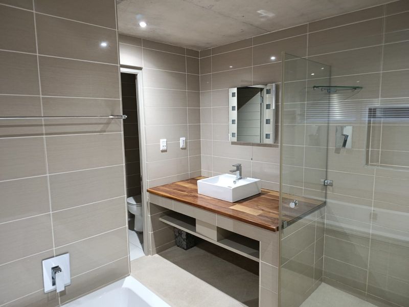 Modern bathroom featuring a timber vanity top with a vessel sink, glass shower enclosure, and neutral wall tiling.