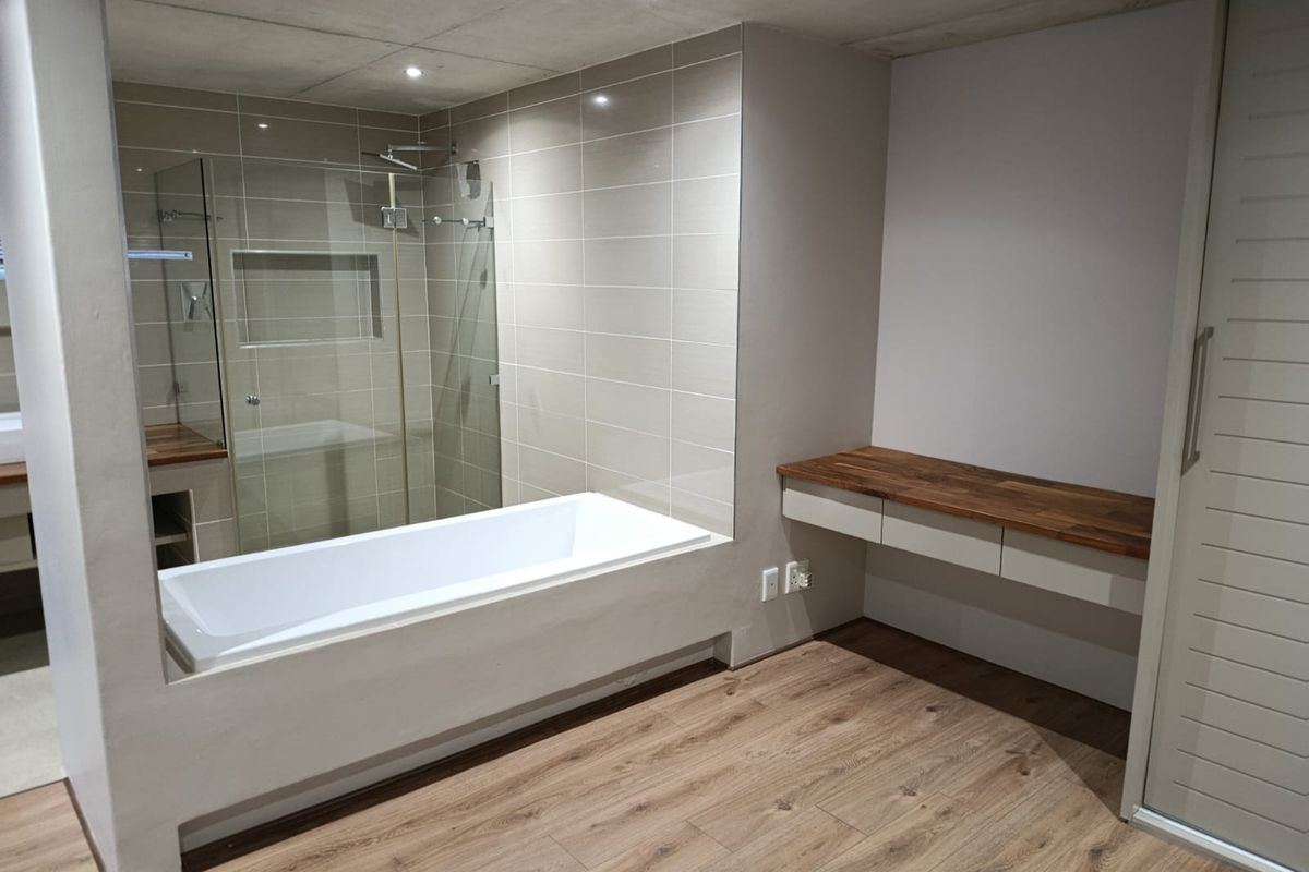 Modern bathroom featuring a built-in bathtub, glass-enclosed shower with a recessed niche, and a sleek floating vanity with a wooden countertop.