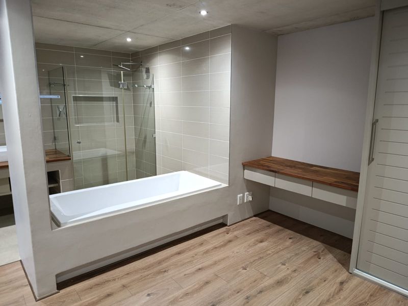 Modern bathroom featuring a built-in bathtub, glass-enclosed shower with a recessed niche, and a sleek floating vanity with a wooden countertop.