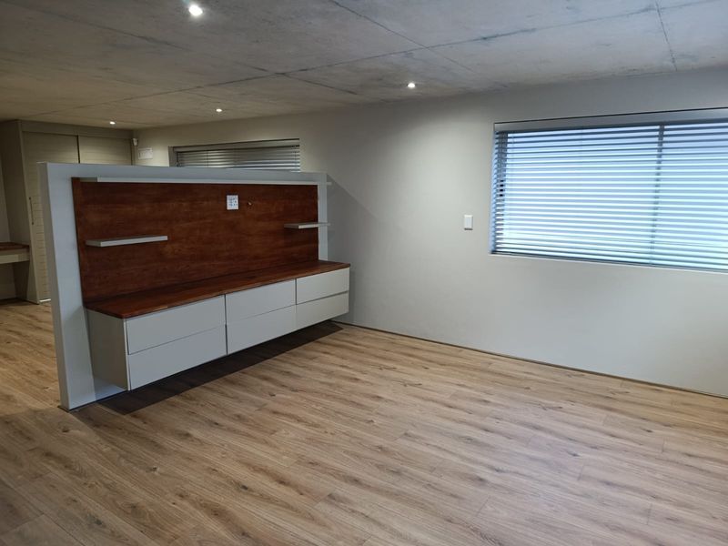 A modern, minimalist bedroom featuring laminate flooring, an exposed concrete ceiling, and custom built-in cabinetry with integrated shelving.