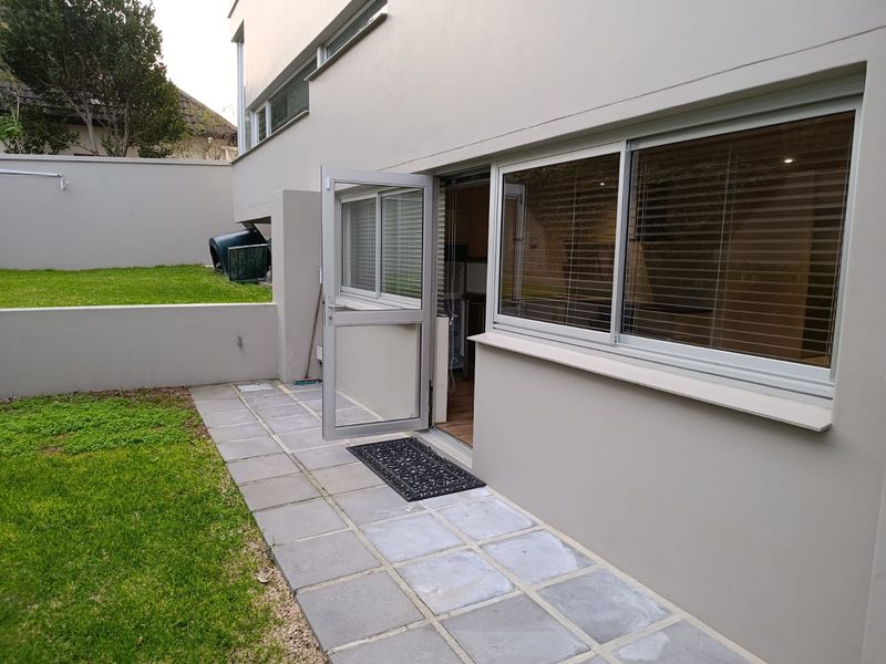 Rear exterior view of the townhouse featuring a paved patio area, small lawn, and direct access through a sliding glass door.