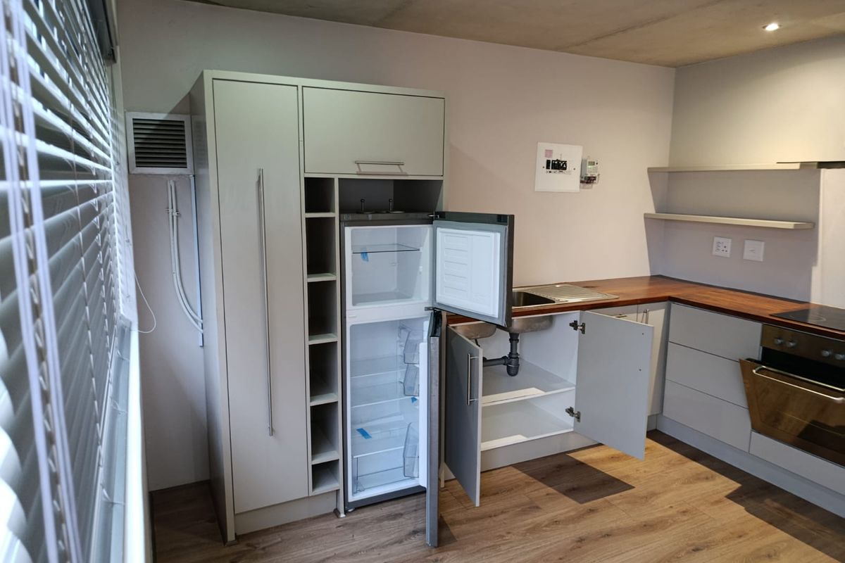 A compact kitchen featuring modern cabinetry, wooden countertops, built-in oven, and laminate flooring. The space is currently vacant and ready for final finishing touches.
