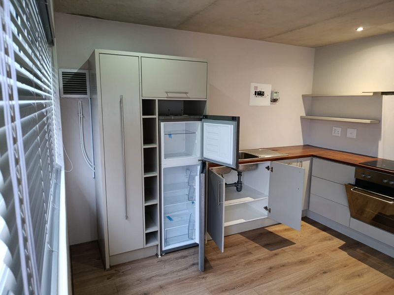 A compact kitchen featuring modern cabinetry, wooden countertops, built-in oven, and laminate flooring. The space is currently vacant and ready for final finishing touches.