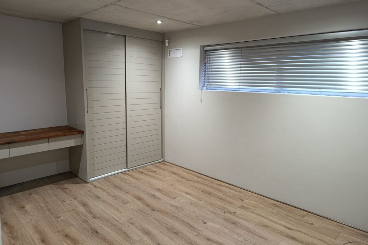 A modern, empty bedroom featuring laminate flooring, a built-in sliding wardrobe, a floating desk, and recessed ceiling lighting.