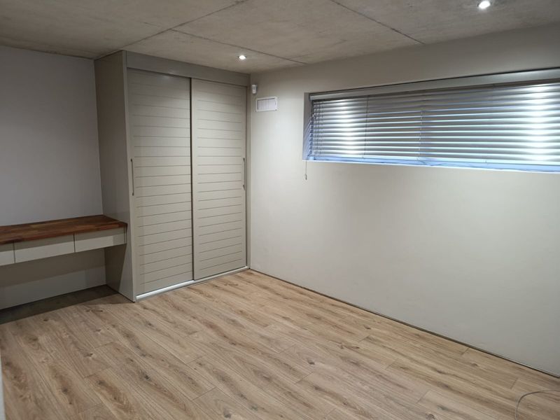 A modern, empty bedroom featuring laminate flooring, a built-in sliding wardrobe, a floating desk, and recessed ceiling lighting.