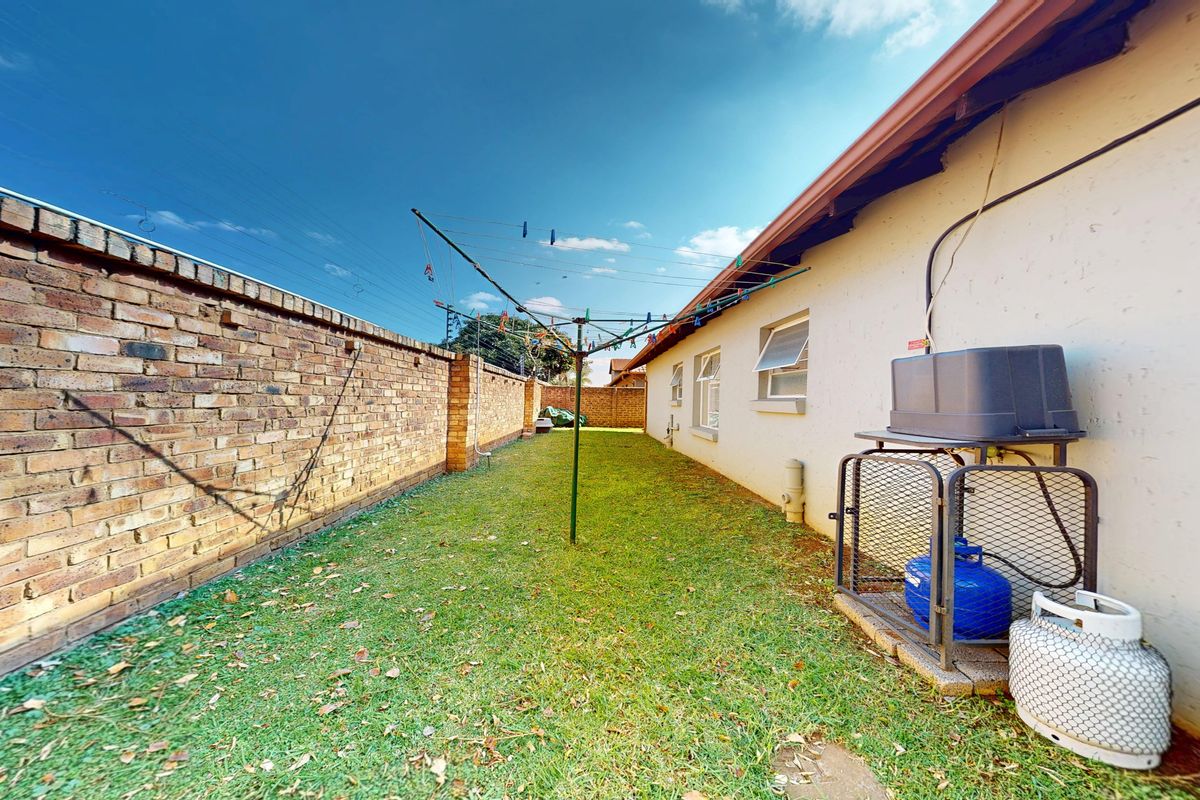 A side garden area featuring a brick boundary wall, a lawn, and a fixed rotary clothesline along the side of the house.