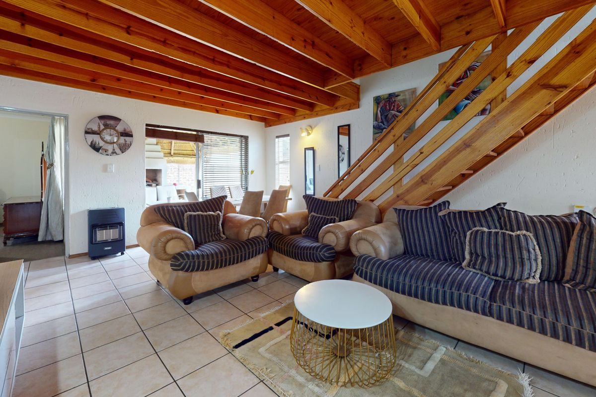 Spacious living room featuring exposed timber ceiling beams, a wooden staircase, and ceramic floor tiles, with direct access to an outdoor patio area.