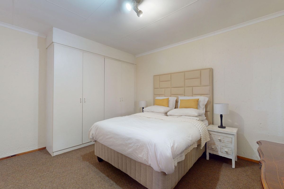 A functional bedroom featuring built-in cupboards, neutral wall finishes, and carpeted flooring, providing a clean and simple living space.