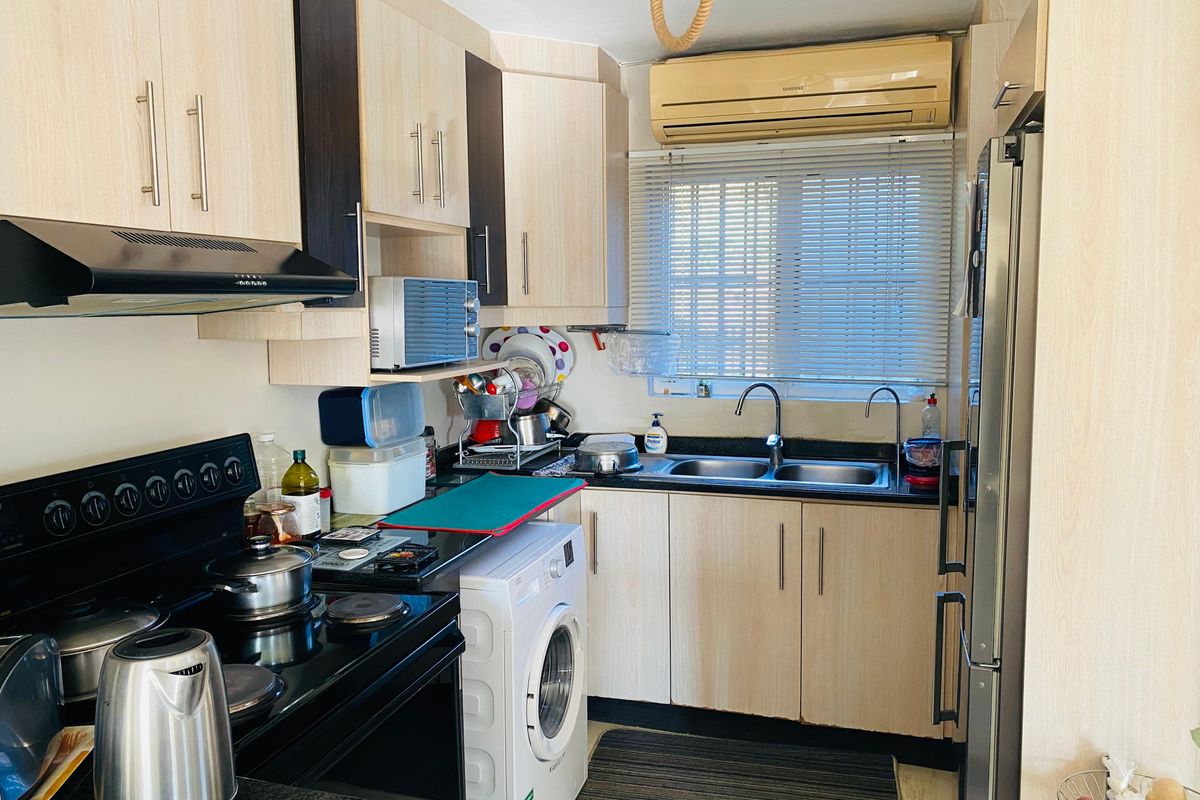 Compact kitchen featuring light wood-tone cabinetry, dark countertops, a double sink, integrated extractor fan, and space for a washing machine.