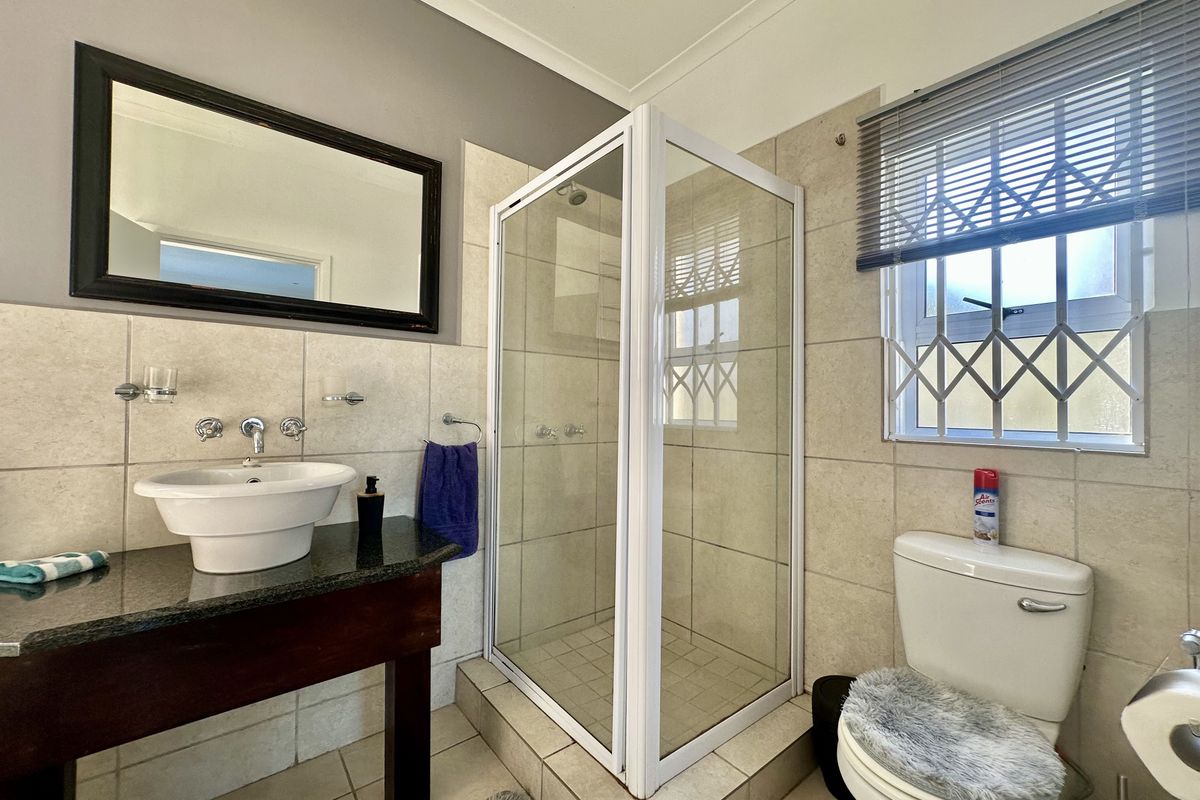 A functional bathroom featuring a shower enclosure, vanity basin with granite countertop, and a toilet, finished with neutral wall tiling.