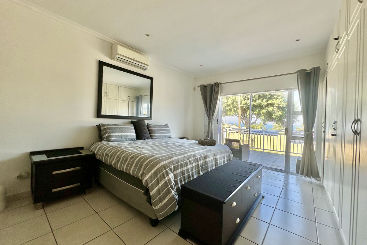 Spacious bedroom featuring tiled flooring, built-in cupboards, a split-system air conditioner, and sliding glass doors leading to an outdoor patio with scenic views.