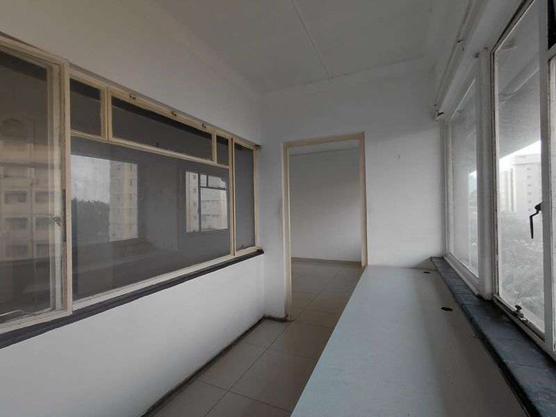An enclosed balcony or sunroom featuring tiled flooring, large windows, and a built-in desk surface, offering a bright and versatile space.