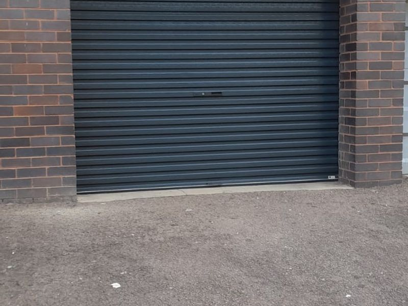 A secure garage entrance featuring a dark roller shutter door, brick pillars, and exterior security lighting.