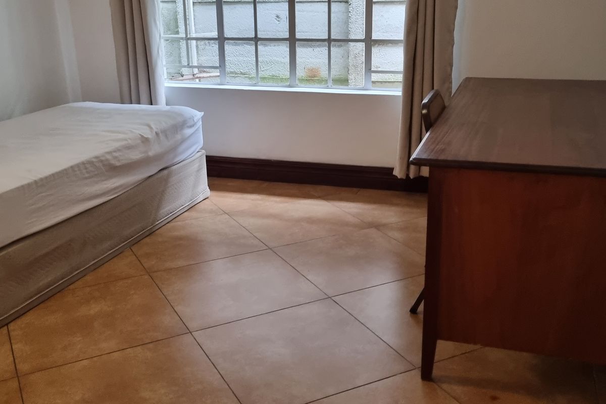 A bedroom featuring tiled flooring and a large grid-pattern window, providing a functional space with neutral finishes.