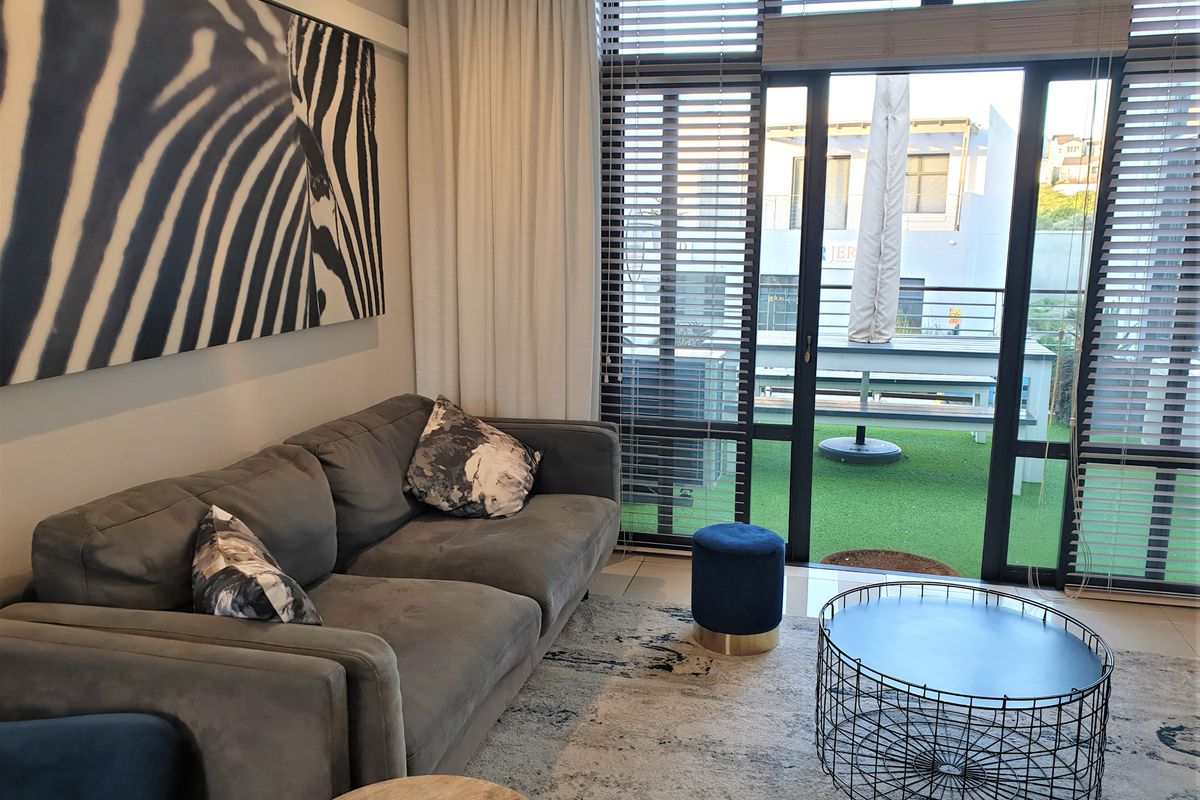 A comfortable living room featuring large floor-to-ceiling windows with integrated blinds, providing direct access to an outdoor patio area.