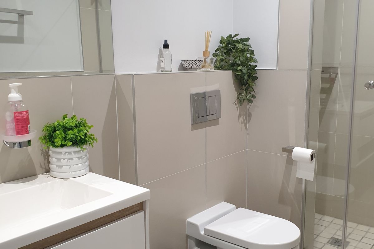Modern bathroom featuring a wall-mounted toilet with concealed cistern, vanity basin, and a glass-enclosed shower with tiled flooring.