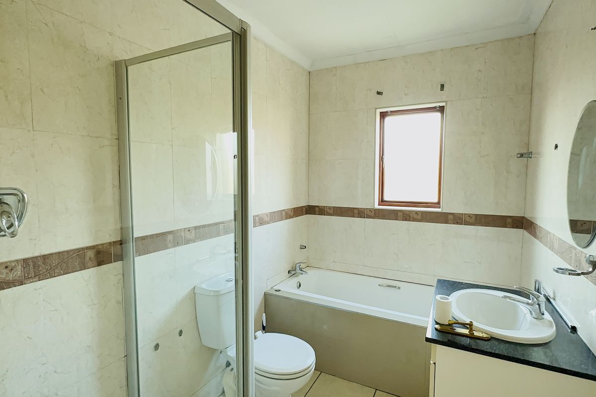 A functional bathroom featuring a shower enclosure, bathtub, vanity basin, and toilet with neutral wall tiling.