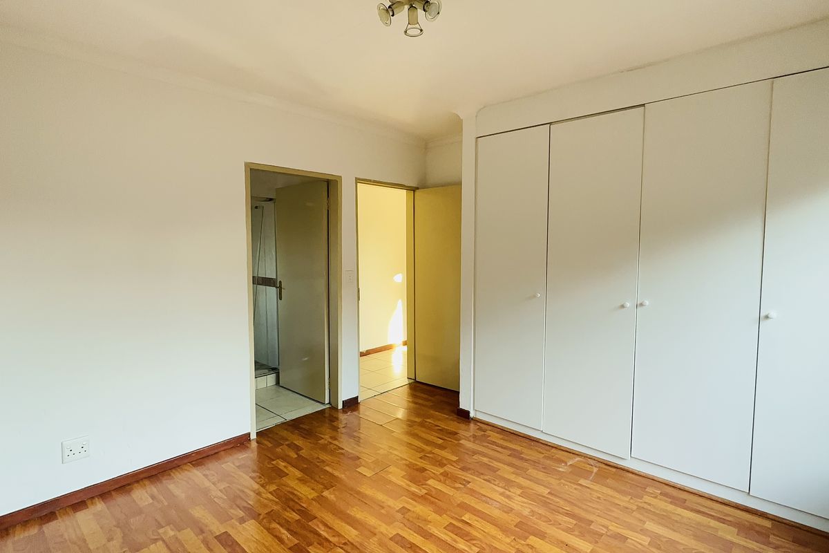 A bright, empty bedroom featuring polished parquet flooring and extensive built-in cupboard storage, with direct access to an en-suite bathroom.
