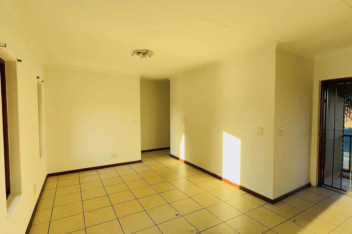 An empty, open-plan living area featuring tiled flooring, neutral walls, and a security gate leading to an outdoor space.