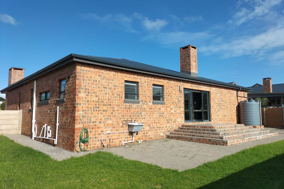 Rear view of a face brick house featuring a paved patio, brick steps, sliding glass doors, and an integrated water storage tank.