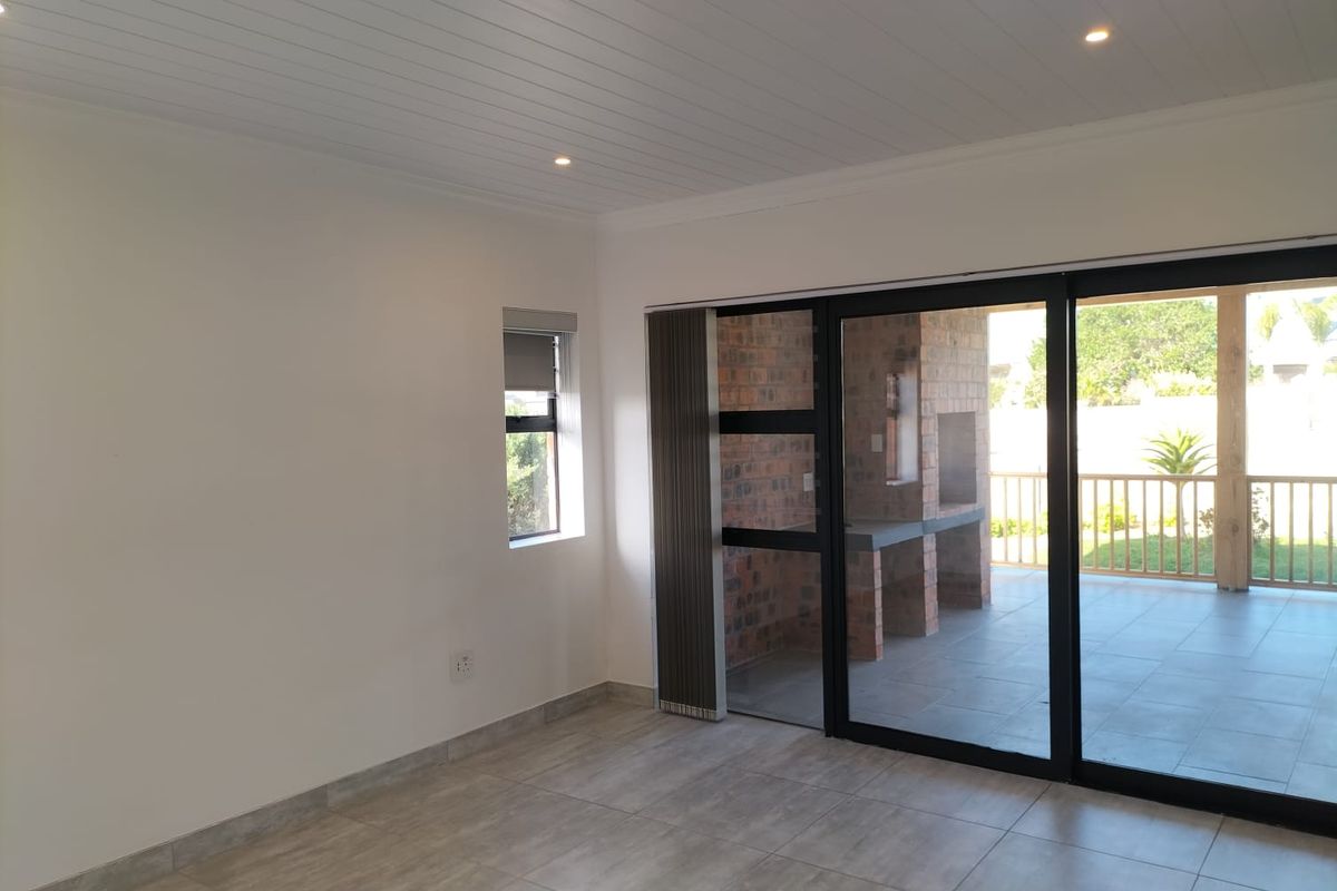 Bright, empty living area featuring tiled floors, recessed lighting, and large sliding doors opening onto a patio with a built-in brick braai.