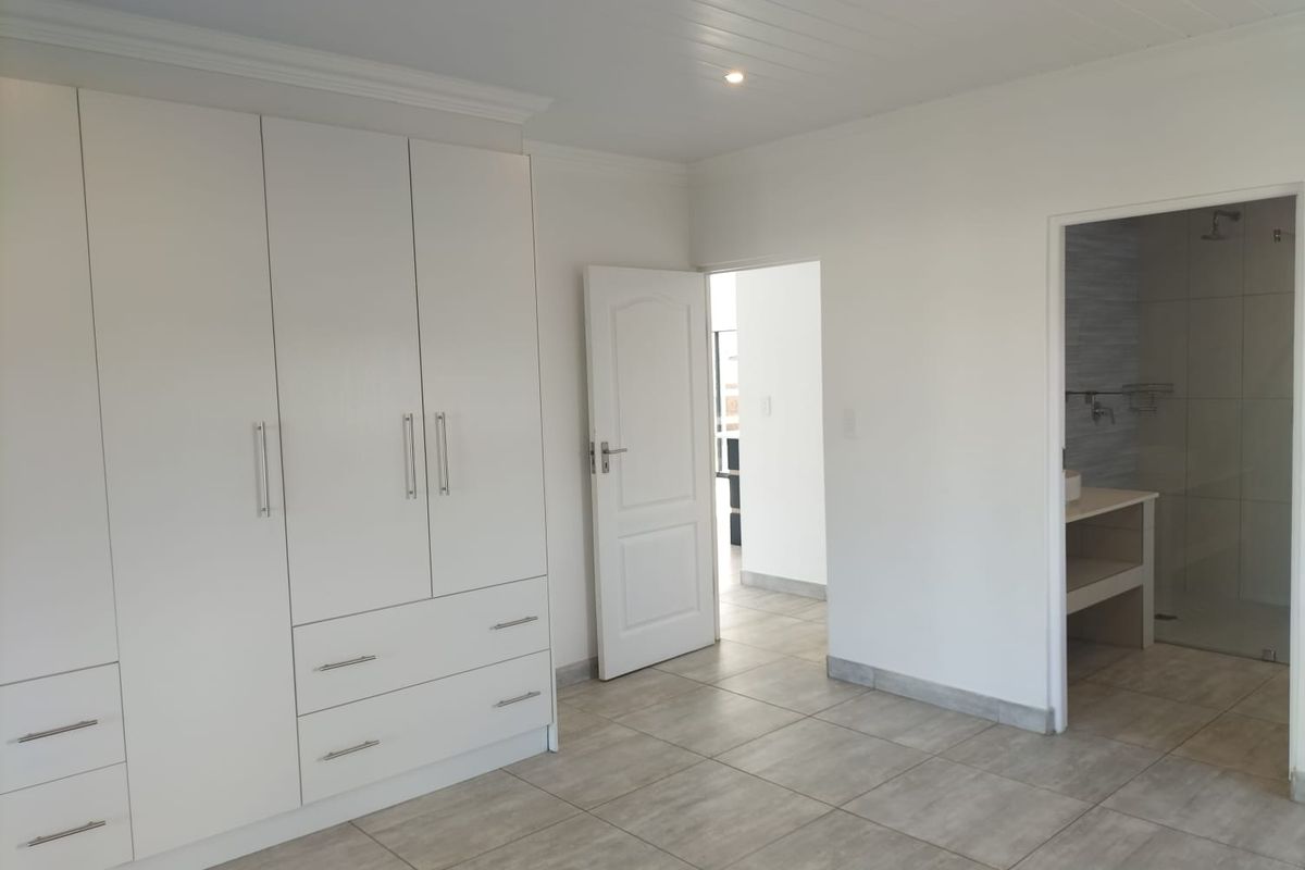 Spacious bedroom featuring neutral tiled flooring, extensive built-in cabinetry, and direct access to an en-suite bathroom with a modern finish.