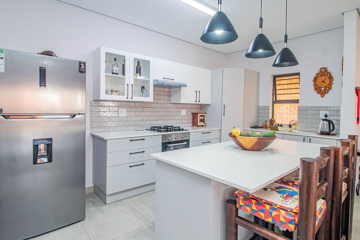Modern kitchen featuring white cabinetry, stone countertops, a central island, gas hob, and stylish pendant lighting, creating a functional and bright cooking space.