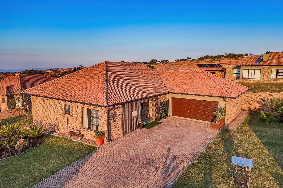 Aerial view of a well-maintained brick house featuring a tiled roof, paved driveway, double garage, and landscaped garden in a residential estate.