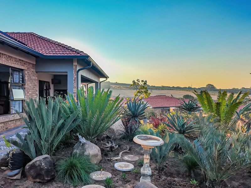 A well-maintained rear exterior view featuring a brick facade, covered patio, and a landscaped garden overlooking a scenic rural landscape.