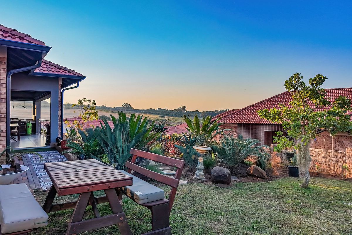 A well-maintained rear garden featuring a covered patio, brick exterior, and scenic landscape views.