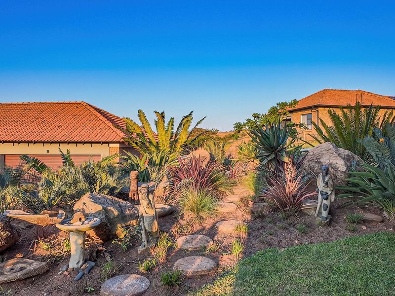 A well-maintained landscaped garden featuring stone pathways, large decorative boulders, and established cycads, set against the backdrop of residential property rooflines.
