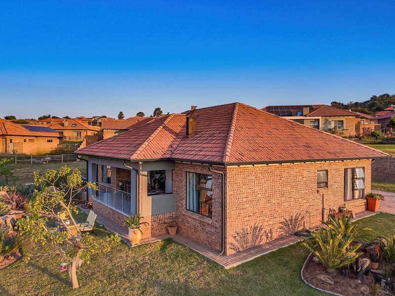 Aerial view of the rear elevation featuring a face-brick facade, tiled roof, and a covered patio area overlooking the landscaped garden.