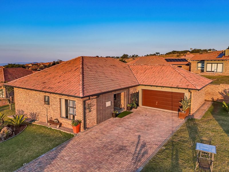 Aerial view of a well-maintained brick house featuring a tiled roof, paved driveway, double garage, and landscaped garden in a residential estate.