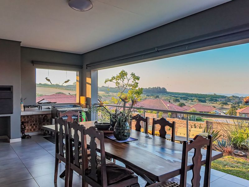 Spacious covered patio featuring a built-in braai, tiled flooring, and expansive views over the surrounding estate.