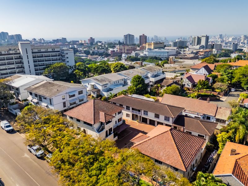 Aerial view of the apartment complex and surrounding urban landscape, showcasing the building layout, tiled roofing, and proximity to city infrastructure.