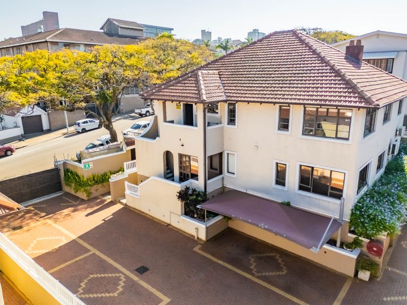 Aerial view of the apartment building exterior, featuring a tiled roof, paved driveway, and covered carport parking area.