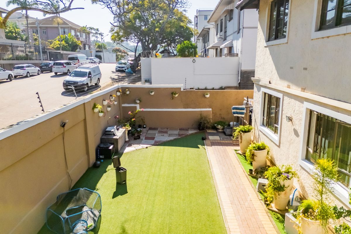 A private rear garden featuring artificial turf, a paved walkway, and high boundary walls, providing a secure outdoor space for the apartment.