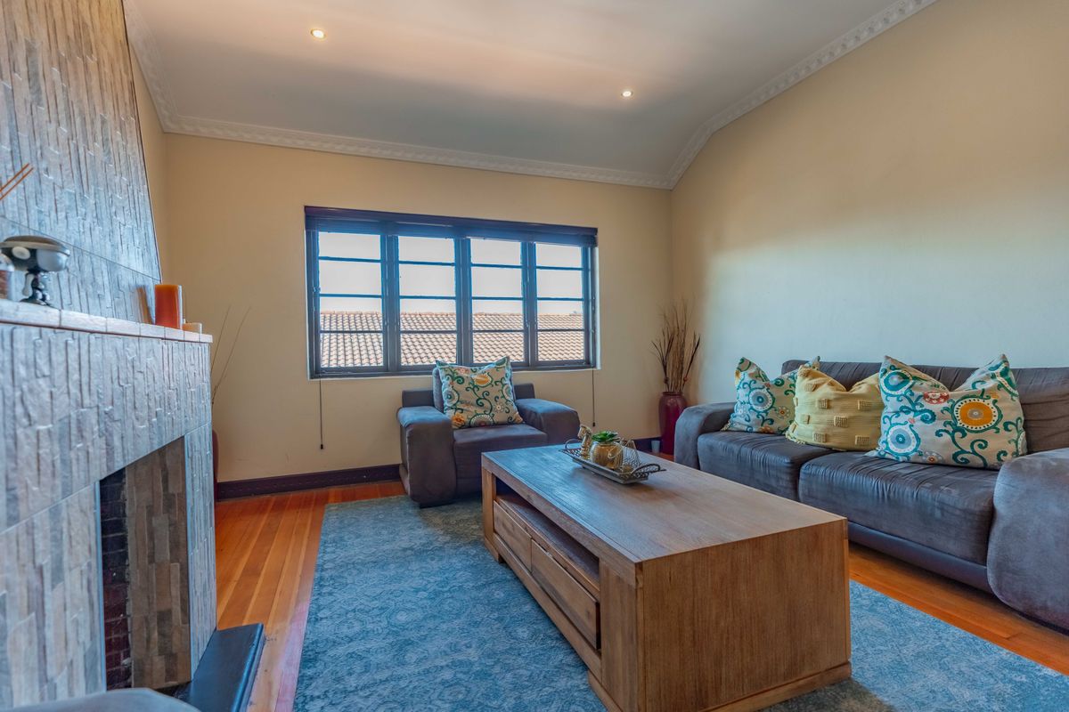 A cozy living room featuring a stone-clad fireplace, hardwood flooring, and large windows that provide natural light.