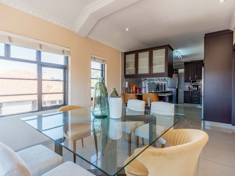 Open plan living and dining area featuring tiled flooring, crown molding, and a modern kitchen with dark cabinetry and integrated breakfast bar.