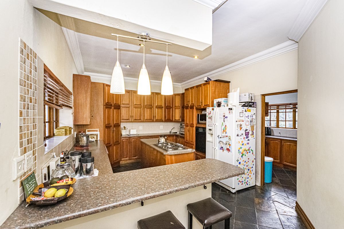 A traditional kitchen featuring wooden cabinetry, a central island with a gas hob, laminate countertops, and tiled flooring, with an adjacent scullery area.