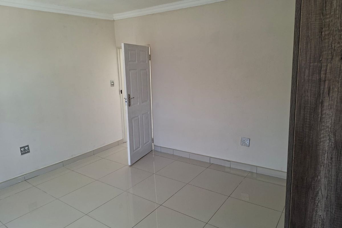 A clean, empty bedroom featuring neutral tiled flooring, coving, and a built-in cupboard, providing a versatile space ready for personalization.