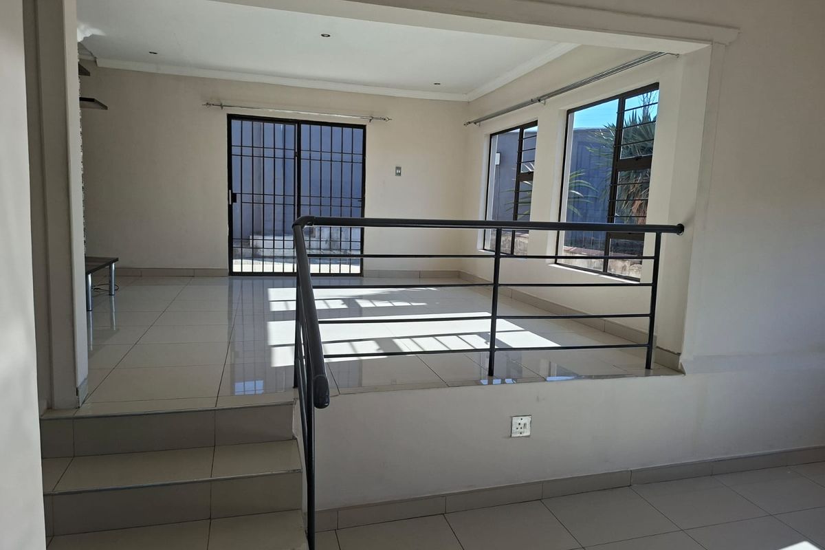 A bright, split-level living area featuring tiled flooring, a metal balustrade, and large windows with access to an outdoor space via a sliding door.
